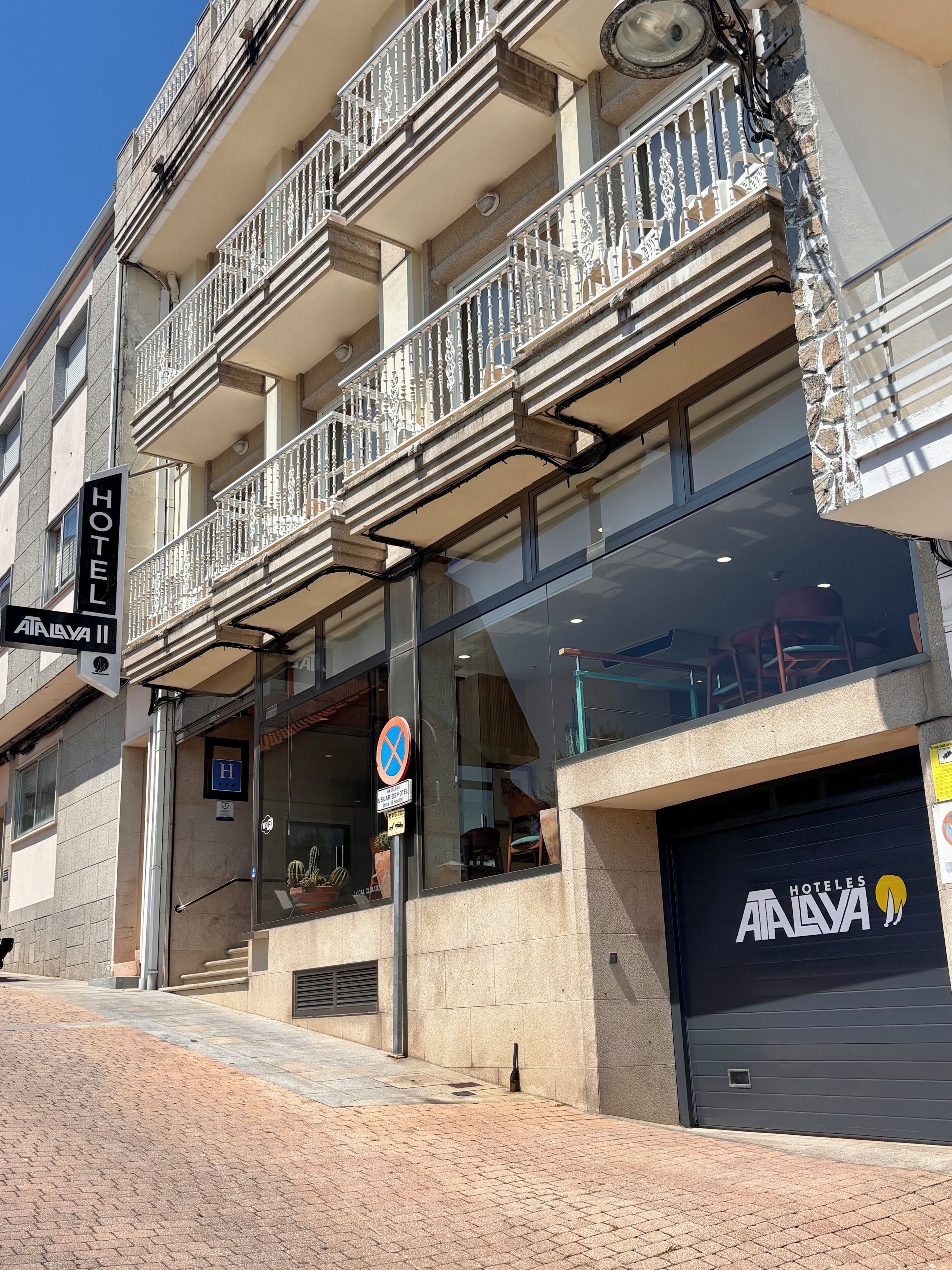 Un hôtel avec une enseigne indiquant « HÔTEL ALAVA », une entrée en verre et un portail de garage fermé.