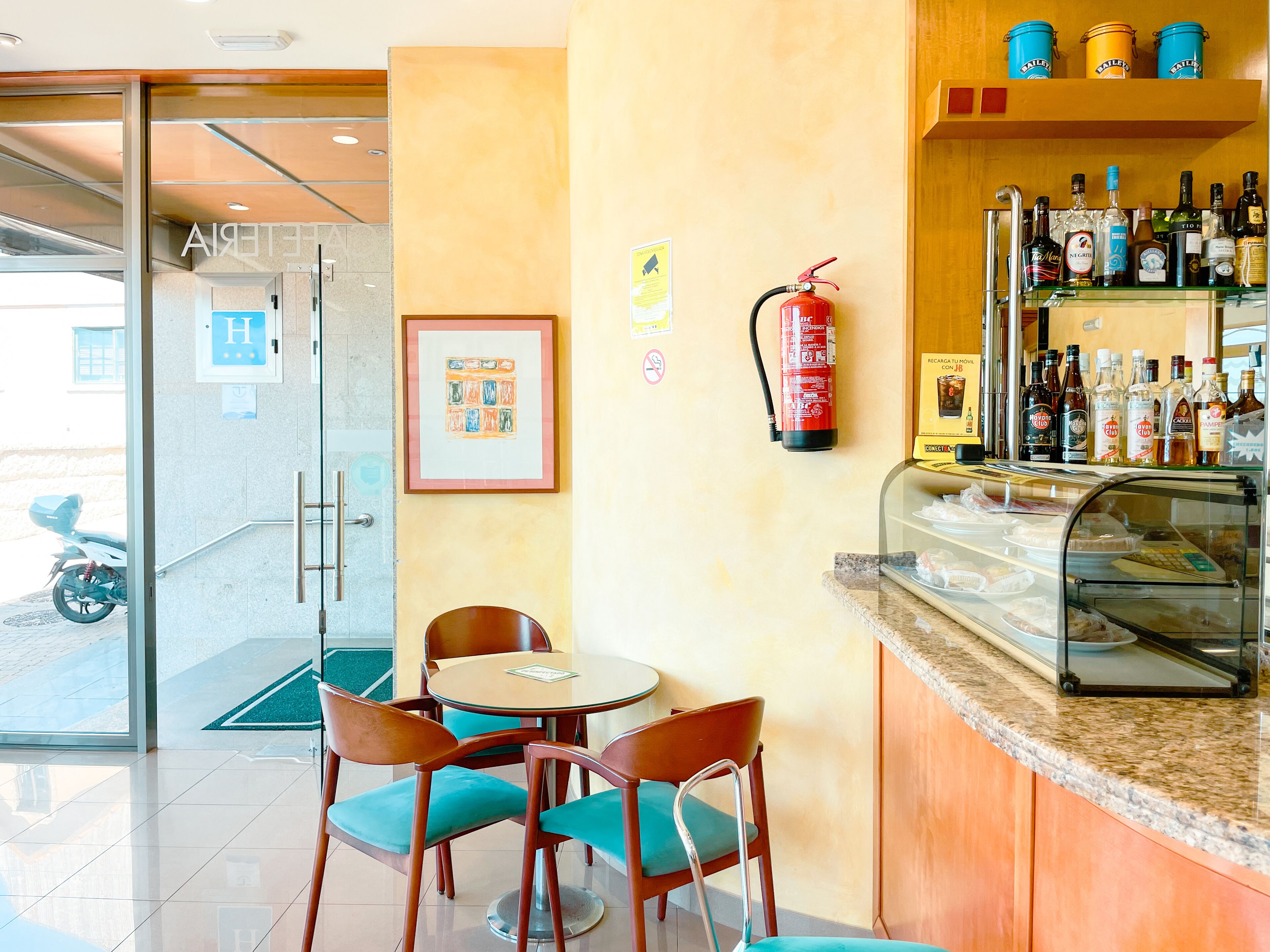 A hotel lobby with a reception desk, chairs, a fire extinguisher, a glass display case with snacks, and a motorcycle outside.