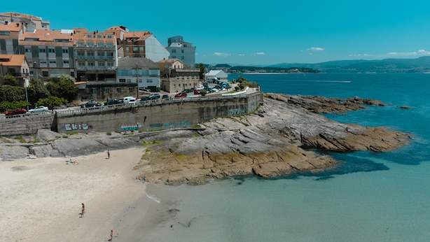 A coastal town with a sandy beach, rocky shoreline, and buildings with balconies overlooking the sea. - Hotel Atalaya II (Sanxenxo)