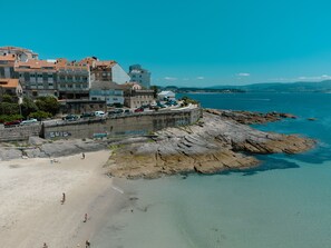 A coastal town with a sandy beach, rocky shoreline, and buildings with balconies overlooking the sea. - Hotel Atalaya II (Sanxenxo)