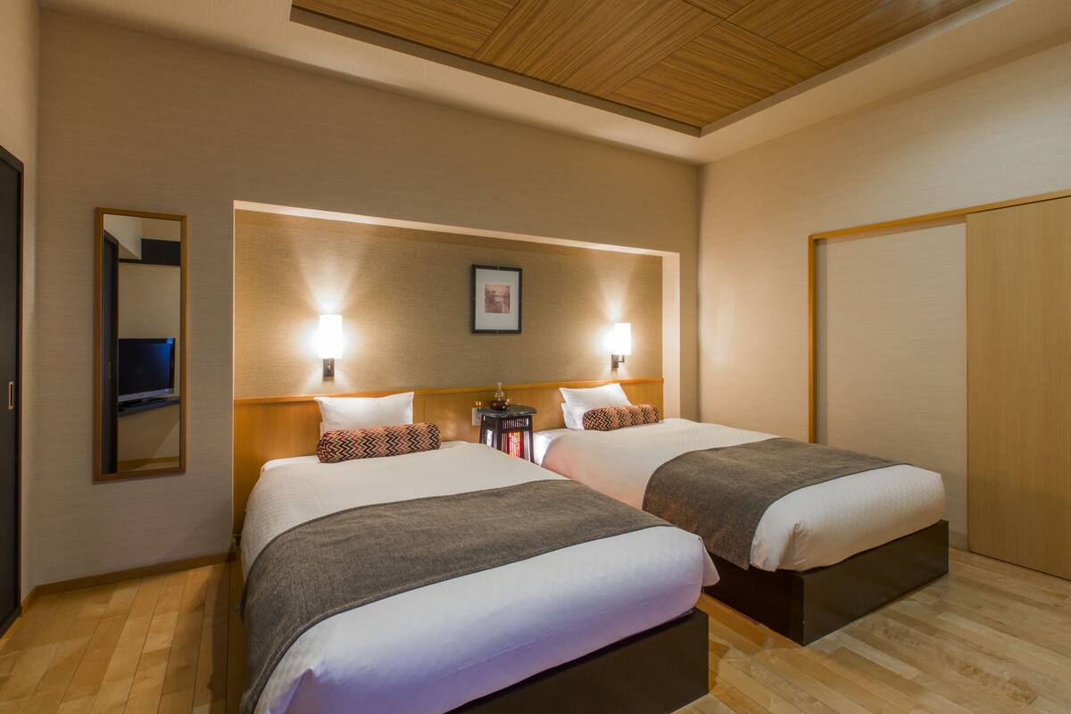 A hotel room with two beds, wooden flooring, a ceiling with wooden paneling, and a framed picture on the wall.