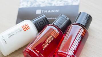Three perfume bottles with labels, one white and two red, placed on a wooden surface with a THANN brand box in the background.
