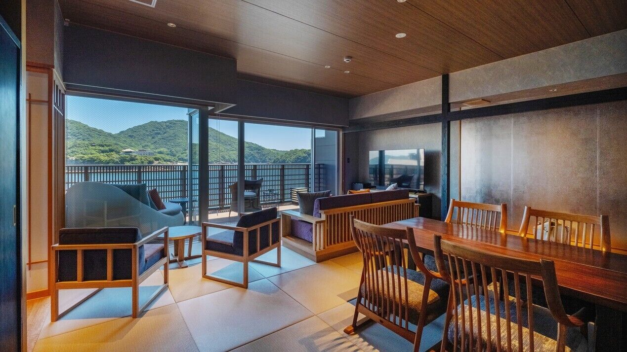 Un intérieur moderne comprenant un coin repas, des sièges et de grandes fenêtres offrant une vue sur un paysage montagneux.