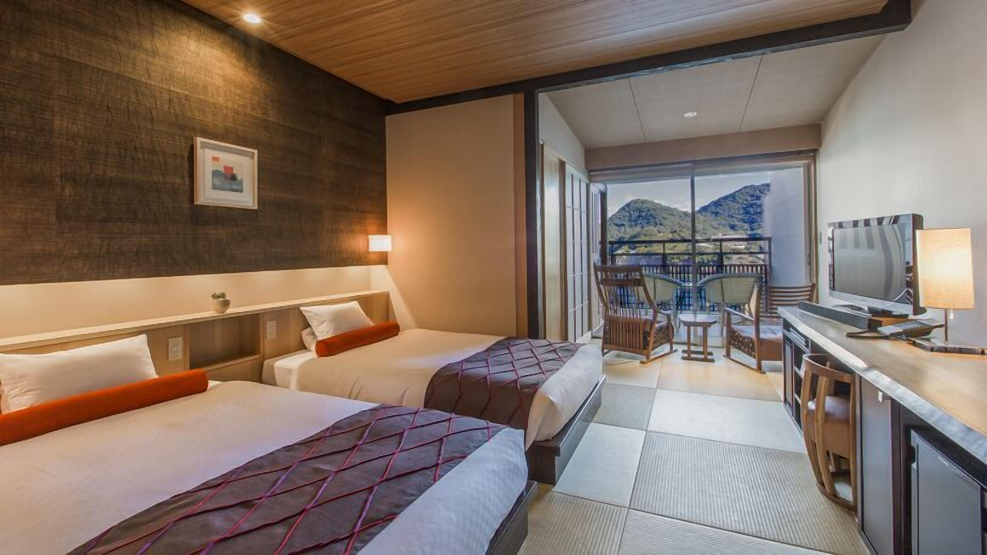 Une chambre d’hôtel avec deux lits, un bureau avec une télévision et un balcon offrant une vue sur la montagne.