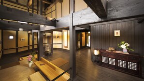 A traditional Japanese interior with wooden beams, tatami flooring, and a reception desk with a vase of flowers. - Migiwatei Ochi Kochi (Fukuyama)