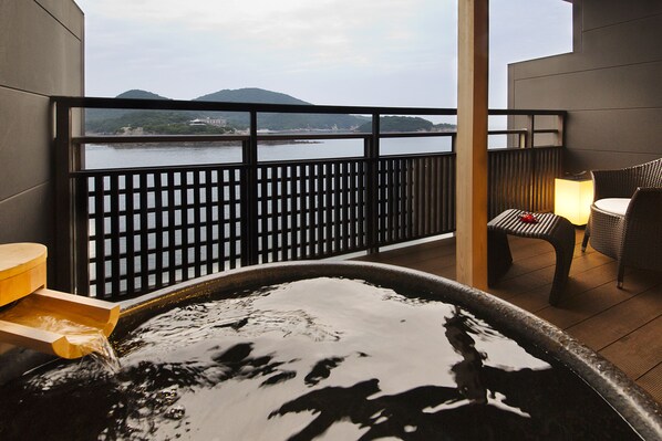 Tinaco con vistas a un cuerpo de agua y montañas a lo lejos, una terraza de madera y mobiliario exterior.