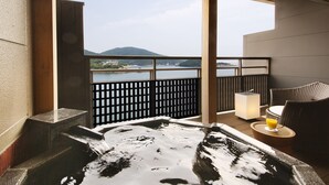 A hot tub with a view of a body of water and mountains, a seating area with a chair and a table, and a small illuminated lamp. - Migiwatei Ochi Kochi (Fukuyama)