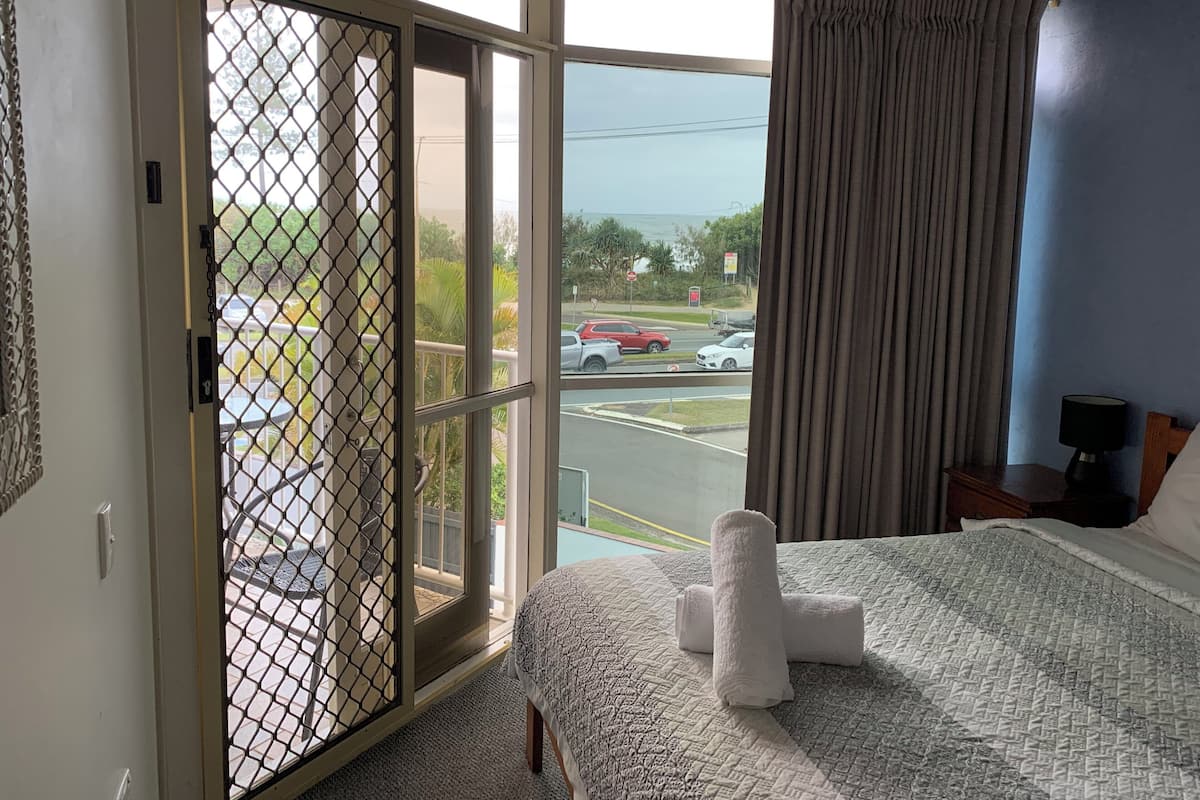 A hotel room with a bed, a window with a view of a parking lot and street, and a sliding door with a mesh screen.