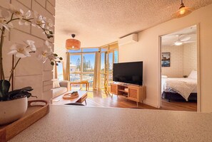 A modern living room with a flat-screen TV, a sofa, a coffee table, and a potted orchid. - Northpoint Holiday Apartments (Alexandra Headland)