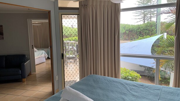 A hotel room with a bed, a ceiling fan, a view of the outdoors, and a balcony with a table and chairs. - Northpoint Holiday Apartments (Alexandra Headland)