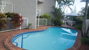 A swimming pool with a tiled edge, surrounded by a brick border, and a white fence. - Northpoint Holiday Apartments (Alexandra Headland)
