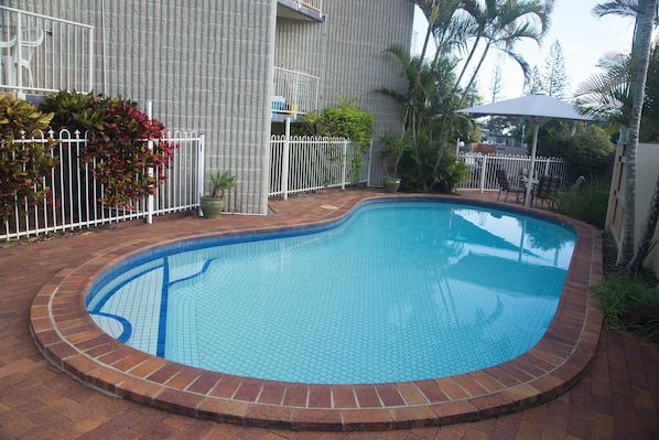 A swimming pool with a tiled edge, surrounded by a brick border, and a white fence. - Northpoint Holiday Apartments (Alexandra Headland)