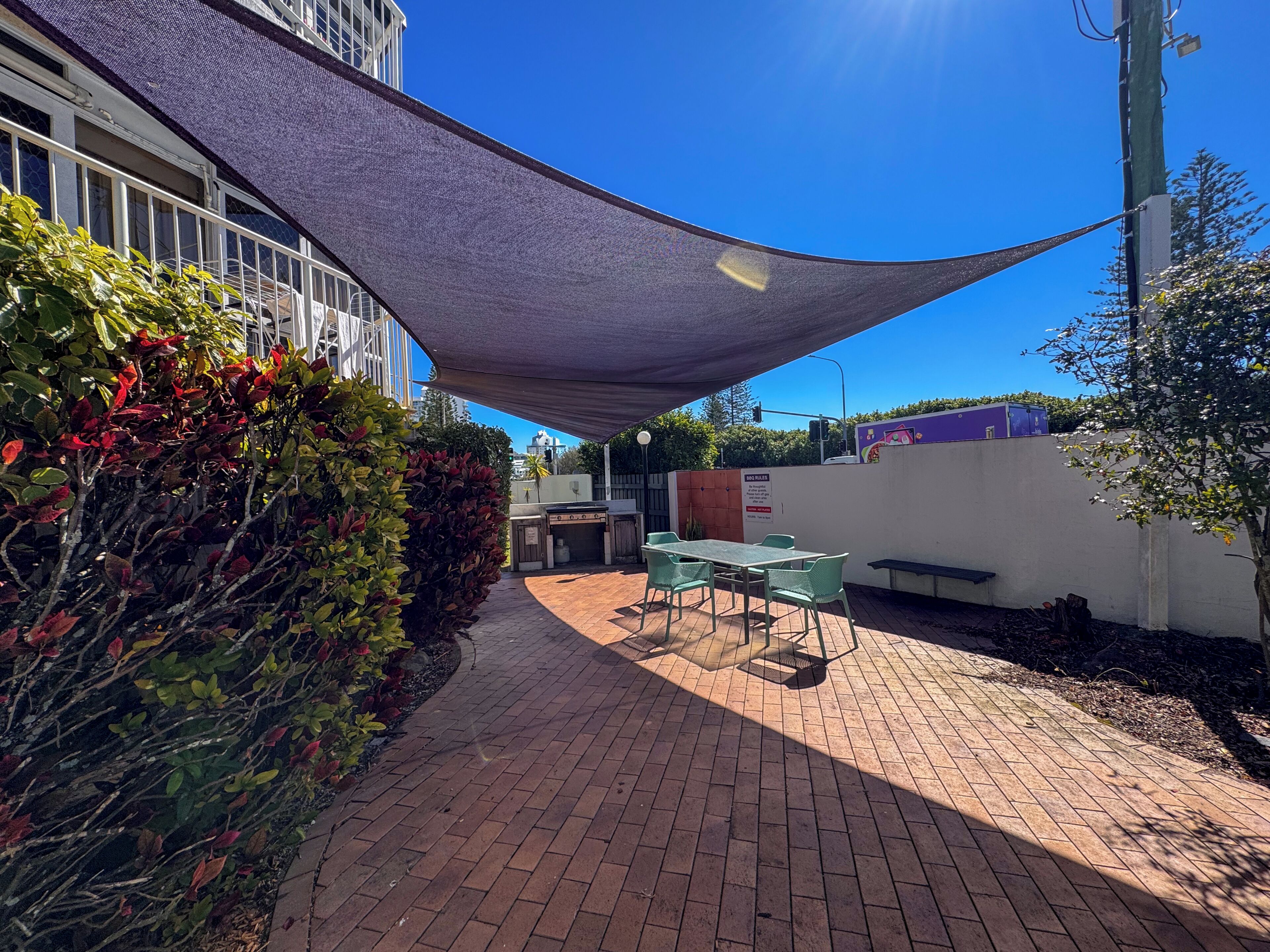 A patio area with a table and chairs, surrounded by a brick walkway and a shaded area.