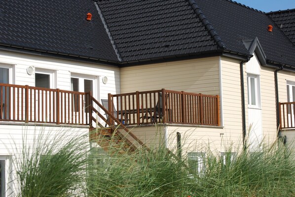 A two-story house with a dark tiled roof, a wooden balcony, and a white exterior. - Evancy Oye Plage (Oye-Plage)