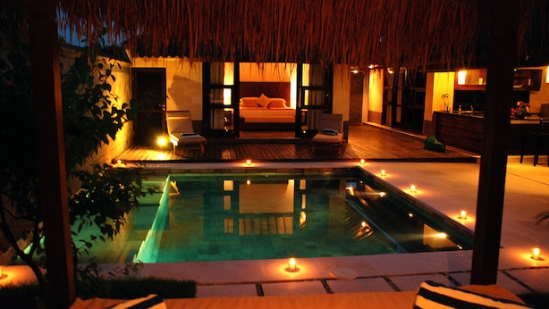 A poolside bedroom with a bed, lounge chairs, and candles. - Gili Villas (Gili Trawangan)