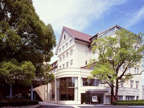 A large, historic building with a prominent corner entrance, large windows, and a red-tiled roof.