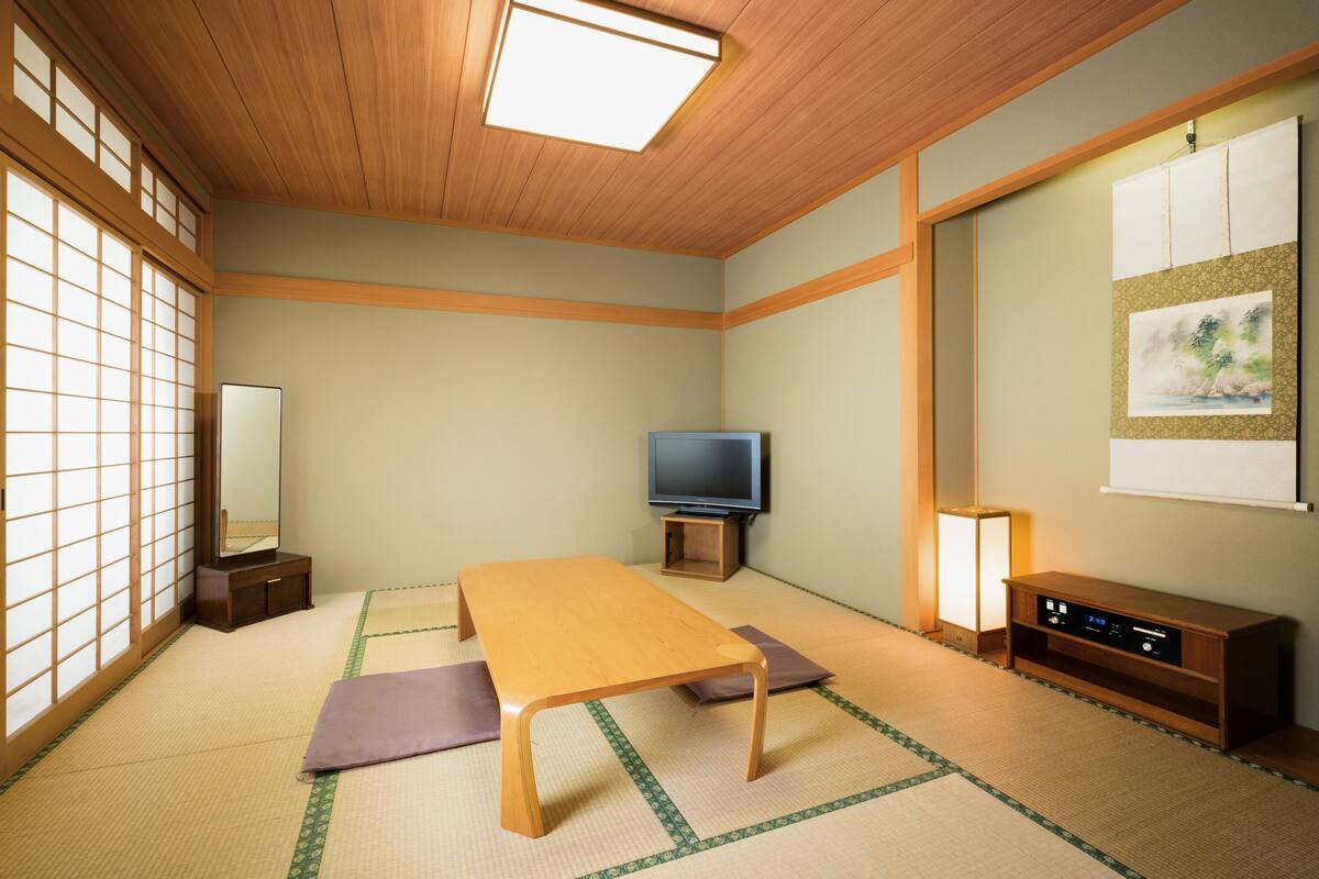 A traditional Japanese room with tatami flooring, a low table, a television, and a cabinet.