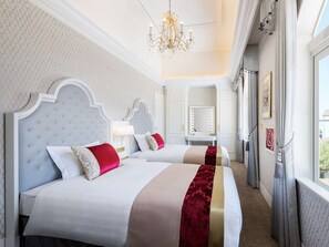 A hotel room with two beds, a chandelier, a mirror, and a view of the outside.