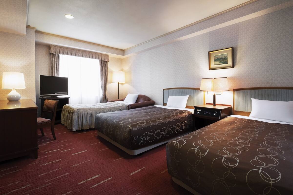 A hotel room with two beds, a TV, a desk, and a lamp.