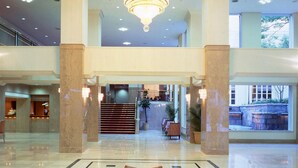 Eine geräumige Lobby mit einem großen Kronleuchter, Marmorböden und einer Treppe zu den oberen Etagen.