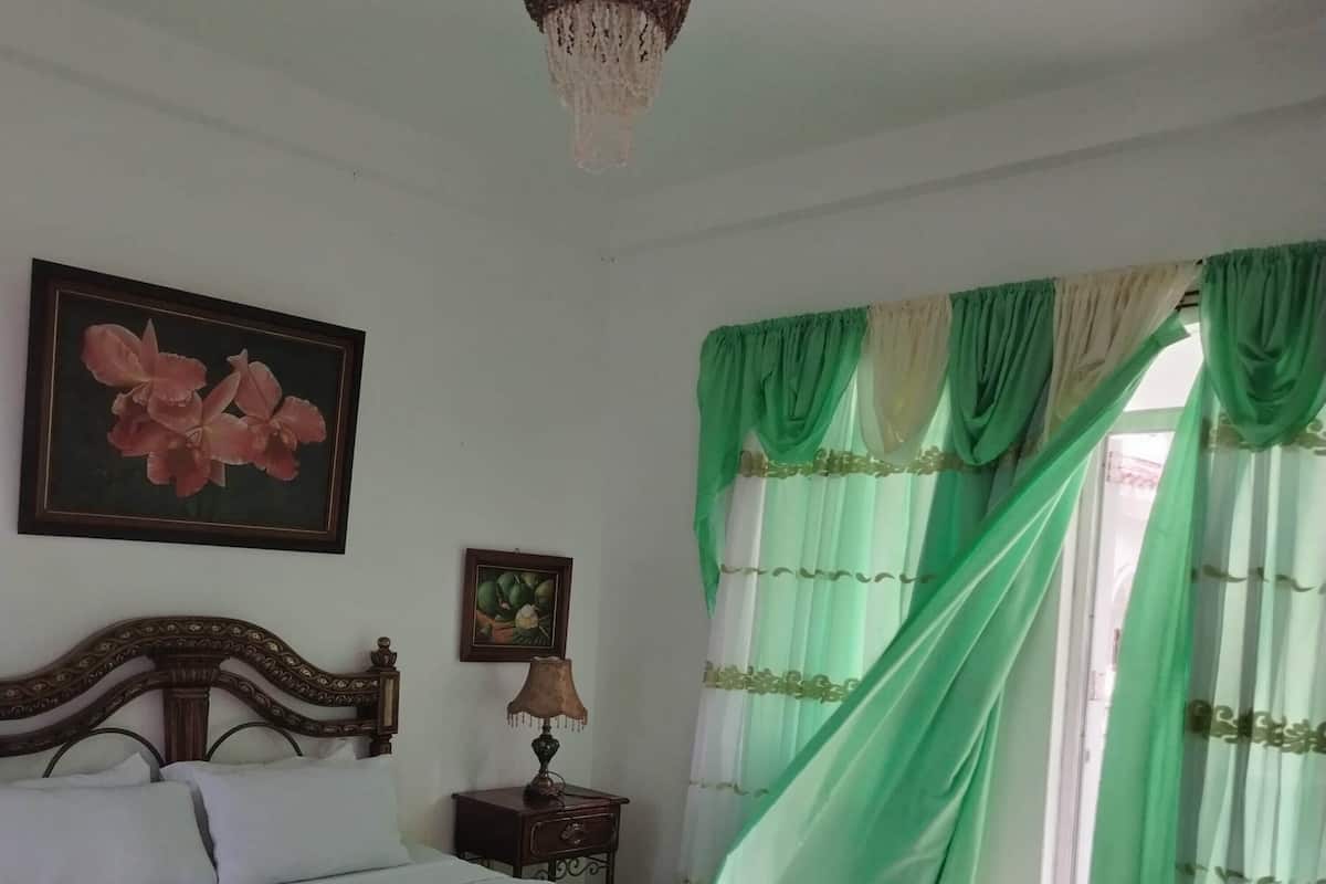 A neatly made bed with a green bed skirt, a wooden headboard, a nightstand with a lamp, and two framed pictures on the wall.