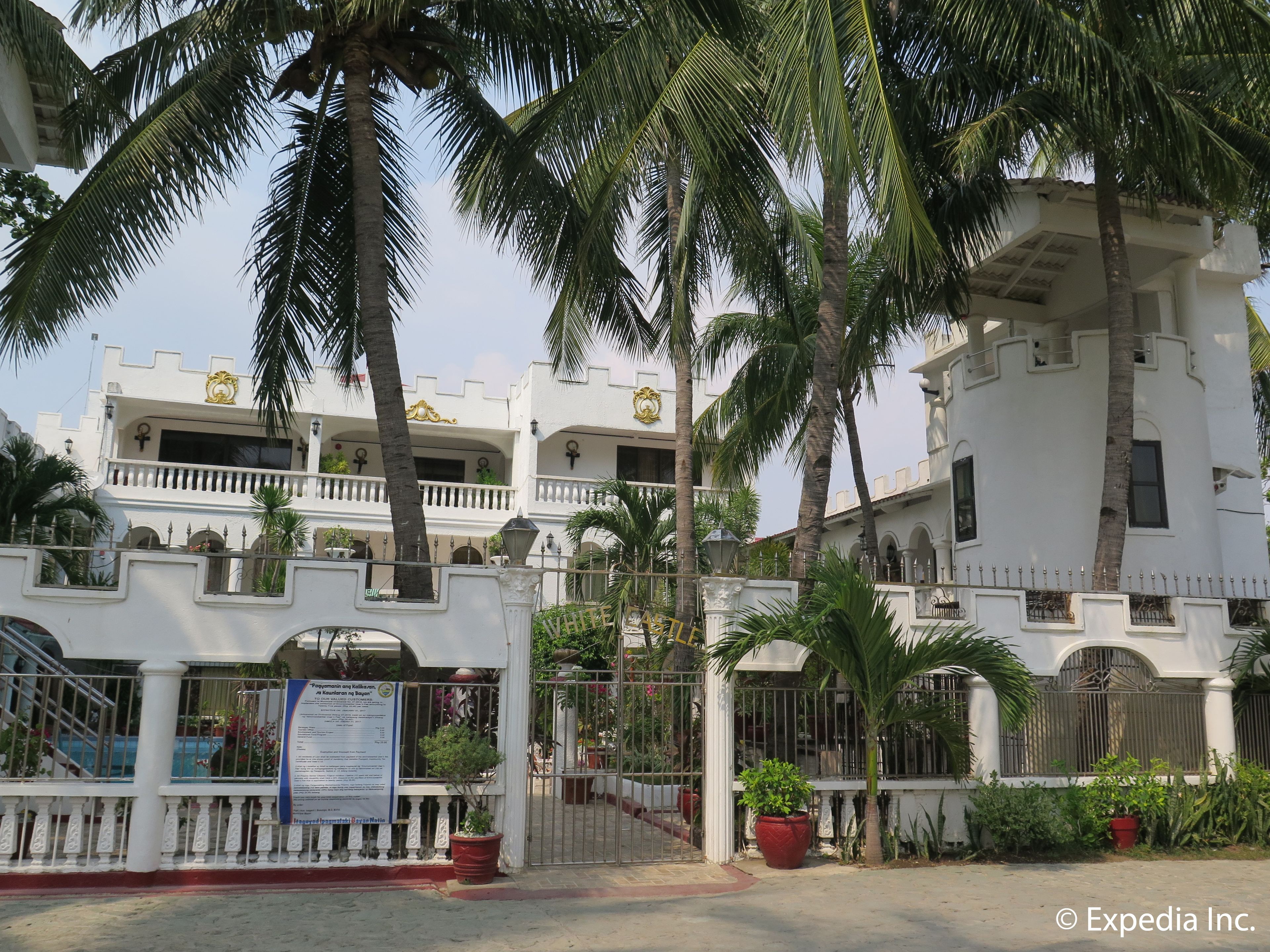 A multi-story building with balconies, palm trees, and a gated entrance.