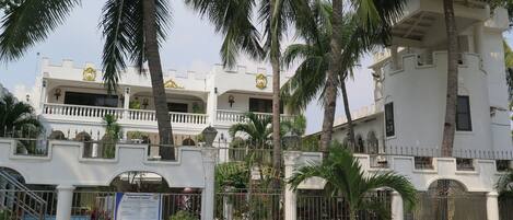 A multi-story building with balconies, palm trees, and a gated entrance.