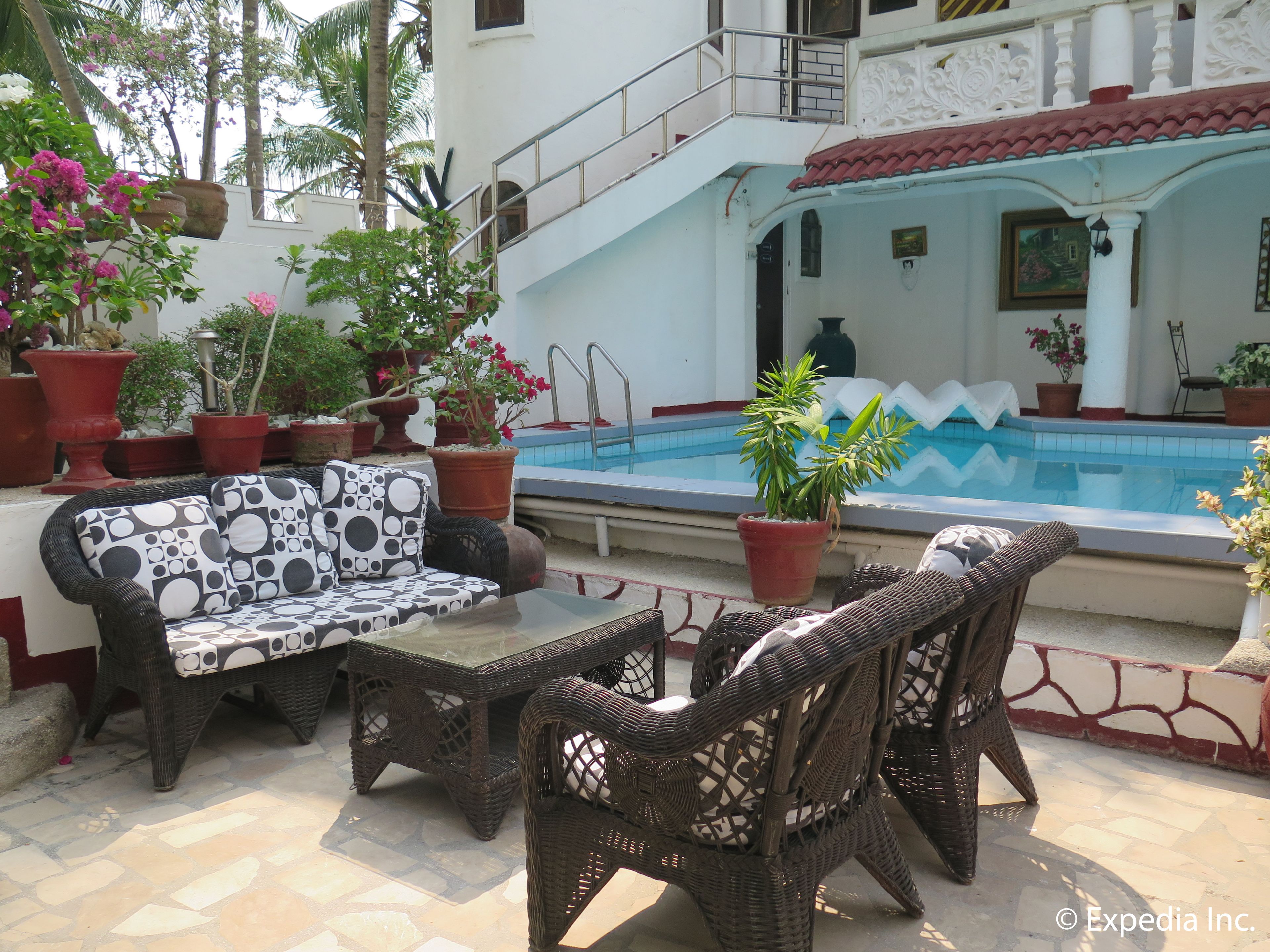 Un área junto a la piscina con muebles de mimbre, plantas en macetas y una piscina.
