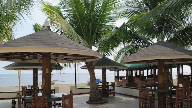 Un restaurante junto a la playa con terraza, palmeras y vista al mar.