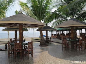 Un restaurante junto a la playa con terraza, palmeras y vista al mar.