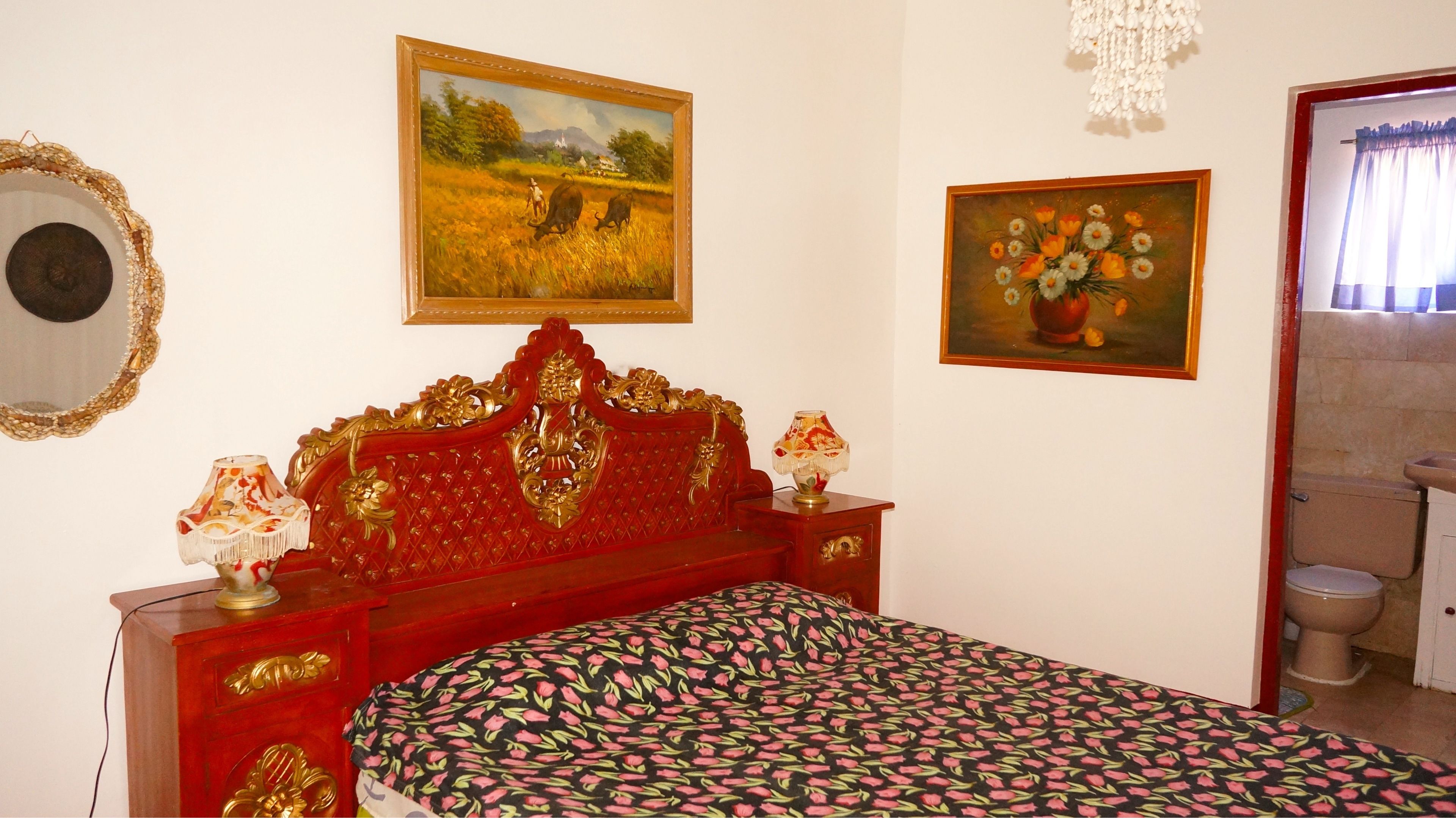Un dormitorio con una cama, un aparador de madera con cajones, un espejo y dos cuadros en la pared.