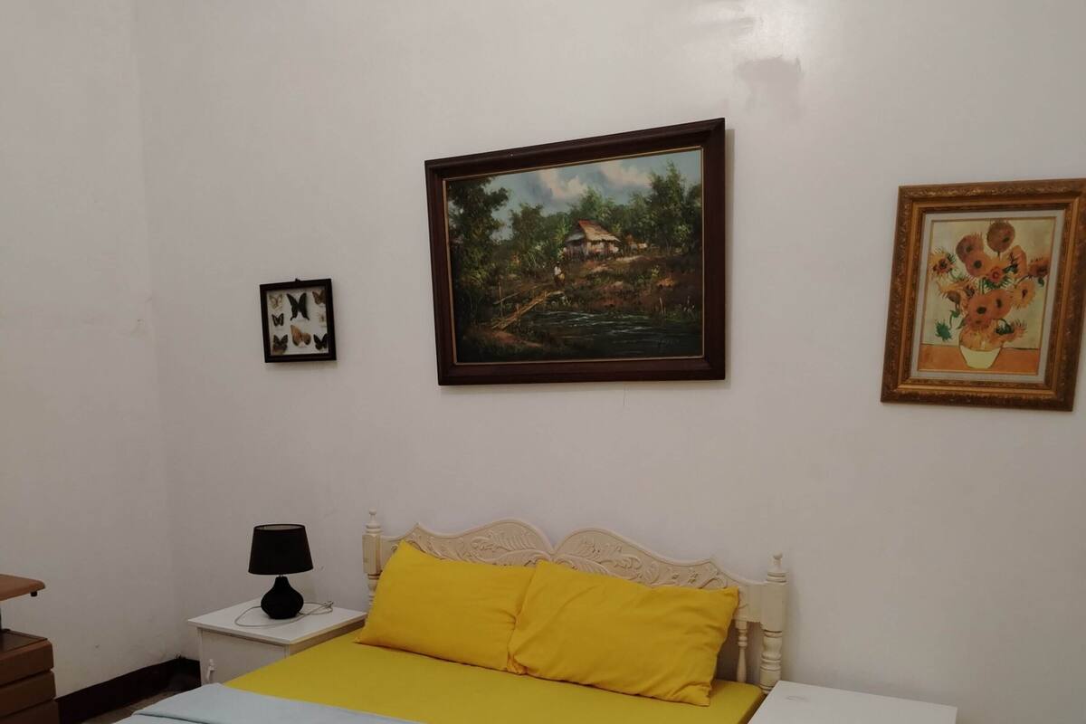 A bedroom with a bed, a nightstand, a lamp, and two framed pictures on the wall.