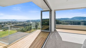 Un balcón moderno con puertas de cristal y suelo de madera, con vistas a un paisaje urbano y montañas.
