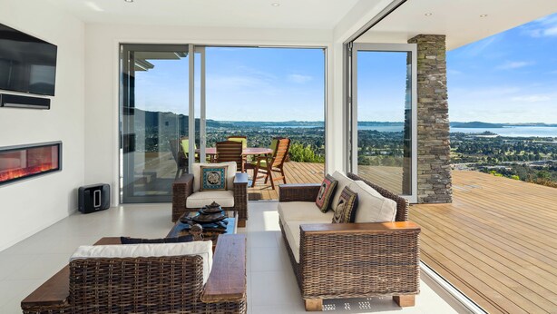 Una sala de estar moderna con muebles de mimbre, una chimenea y un amplio ventanal que da a una terraza con vistas panorámicas.