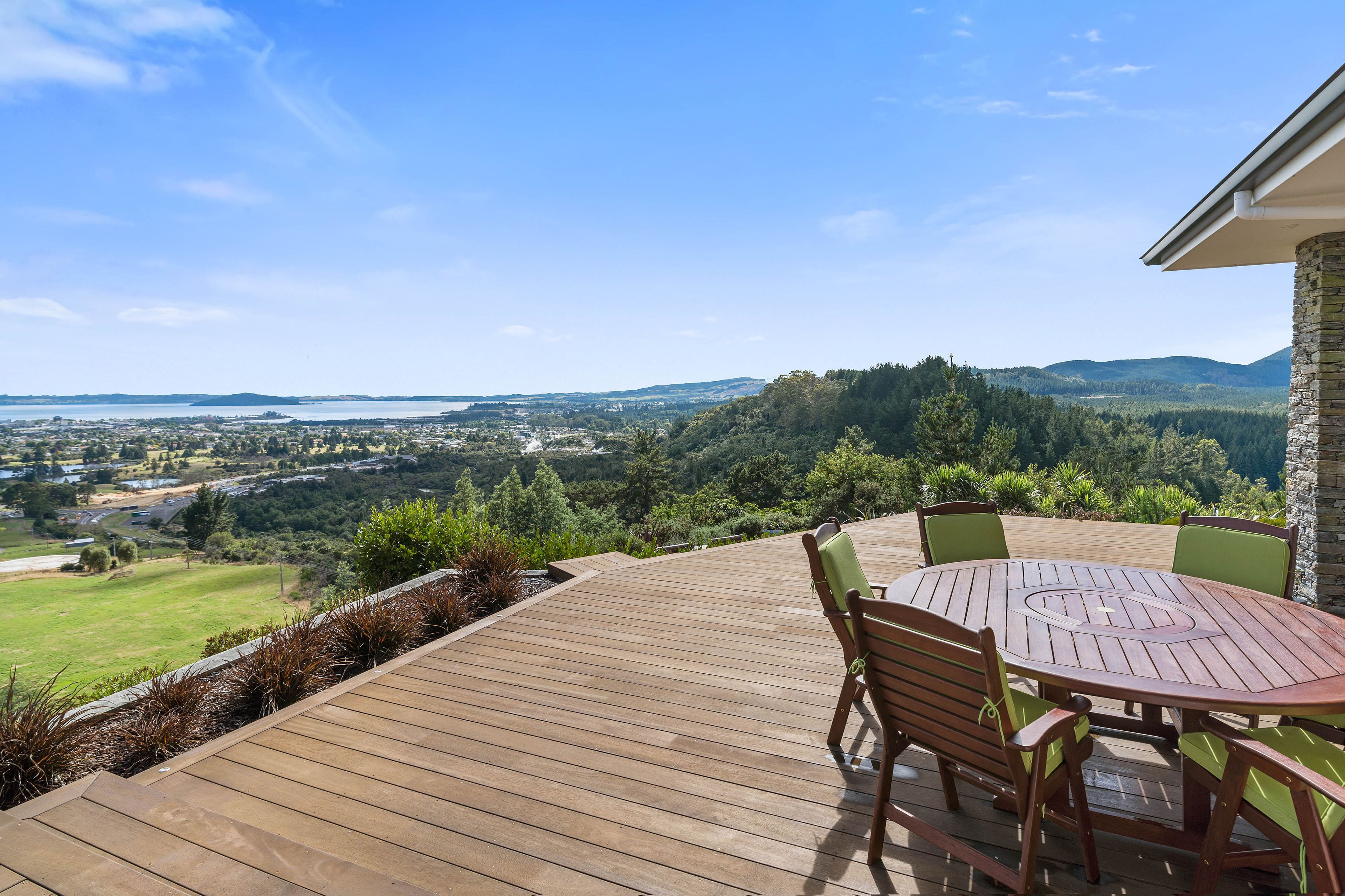 A wooden deck with a round table and chairs, overlooking a scenic landscape with hills and a body of water.