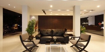 Un vestíbulo moderno con un sofá de cuero, dos sillones, una mesa de centro de vidrio y un mostrador de recepción.