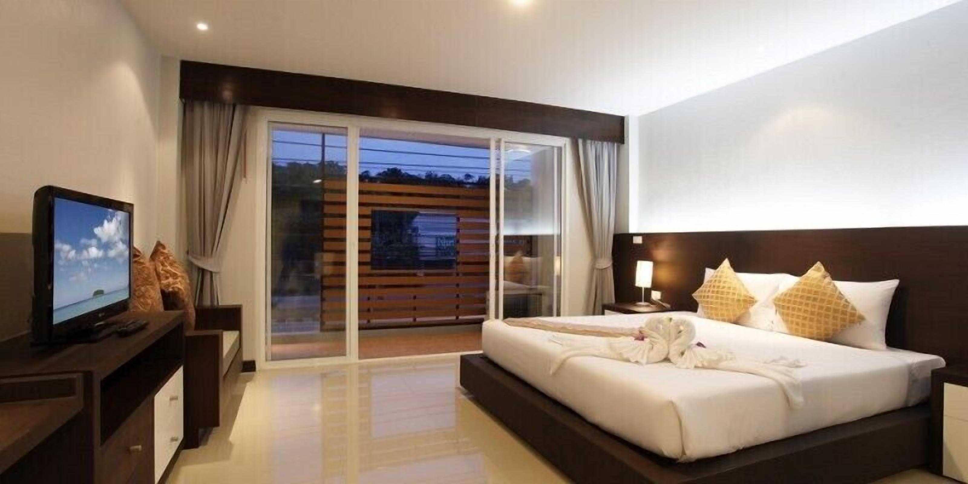 A hotel room with a bed, a TV, a desk, and a view of the outdoors.