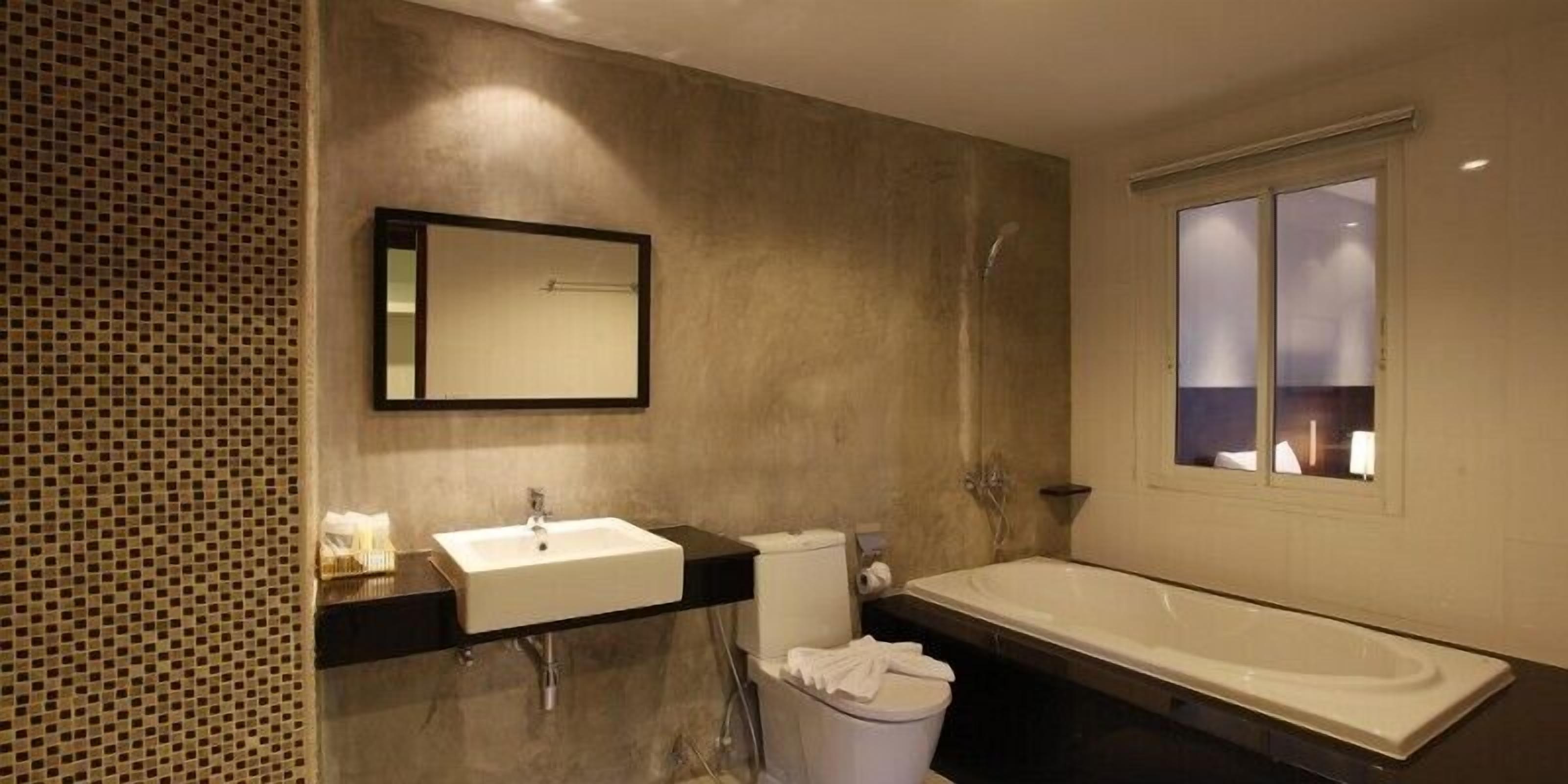 A modern bathroom with a large mirror, a sink, a toilet, and a bathtub.