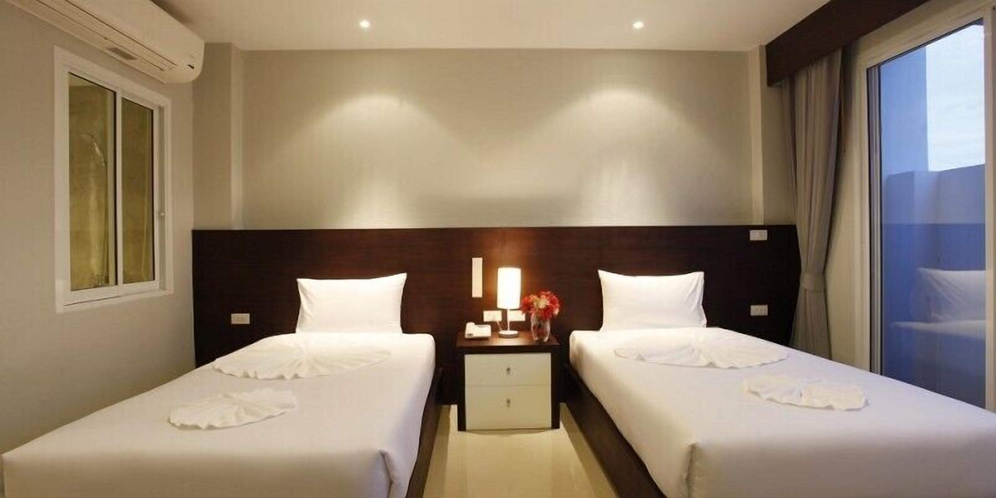 Habitació d'hotel amb dos llits, una tauleta de nit amb una làmpada i una finestra amb cortines.