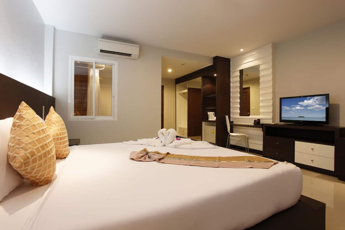A hotel room with a neatly made bed, a television, a mirror, and a bathroom visible through an open door.