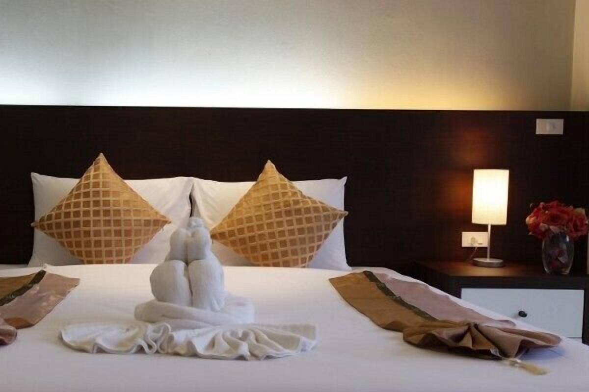 A neatly made bed with two pillows, a bedside lamp, and a vase with flowers.