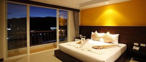 Un cuarto de hotel con una cama grande, una mesita de noche y vistas de la ciudad al atardecer.