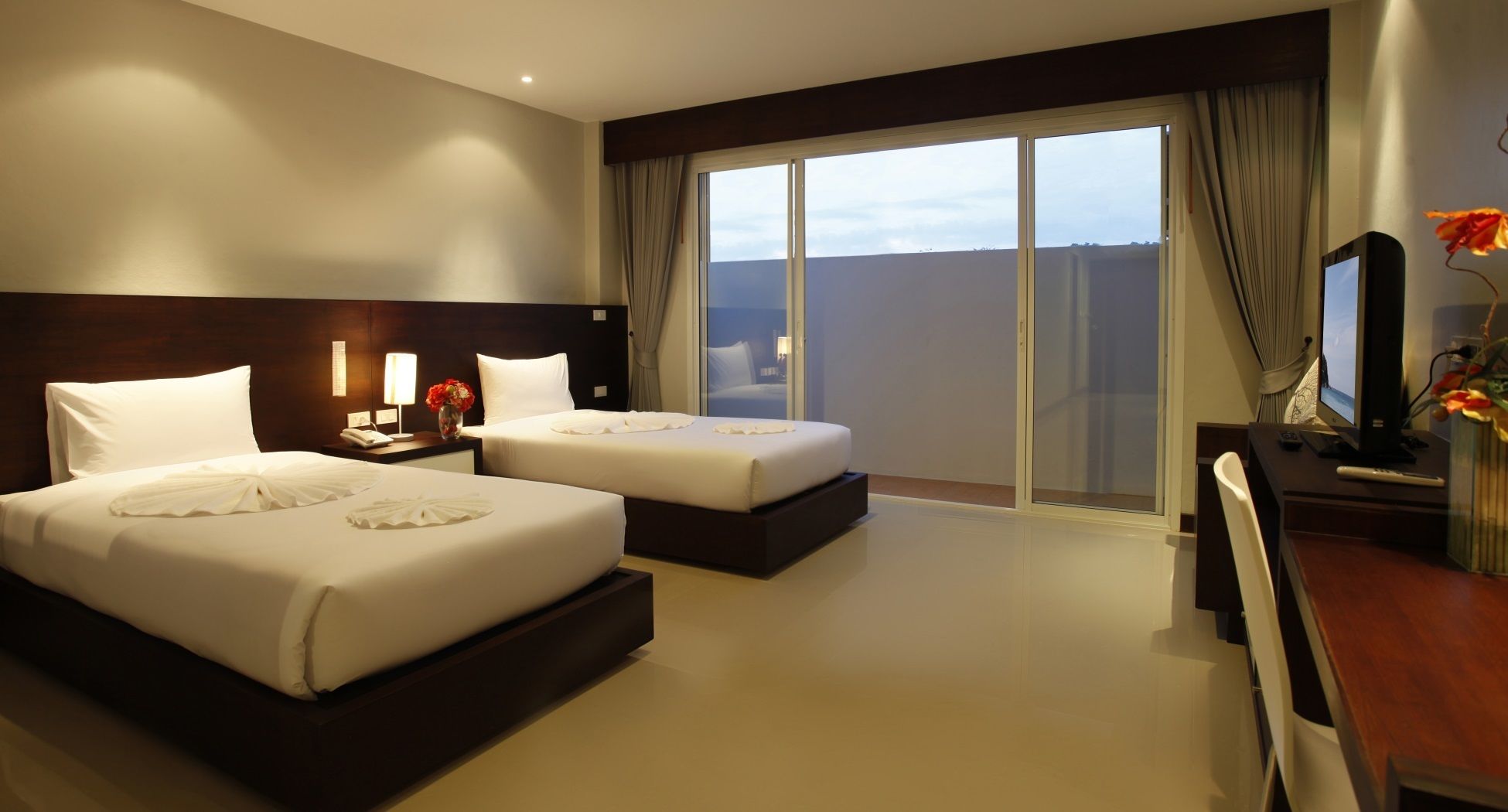 Habitación de hotel con dos camas, un escritorio, un televisor y un ventanal con vistas.