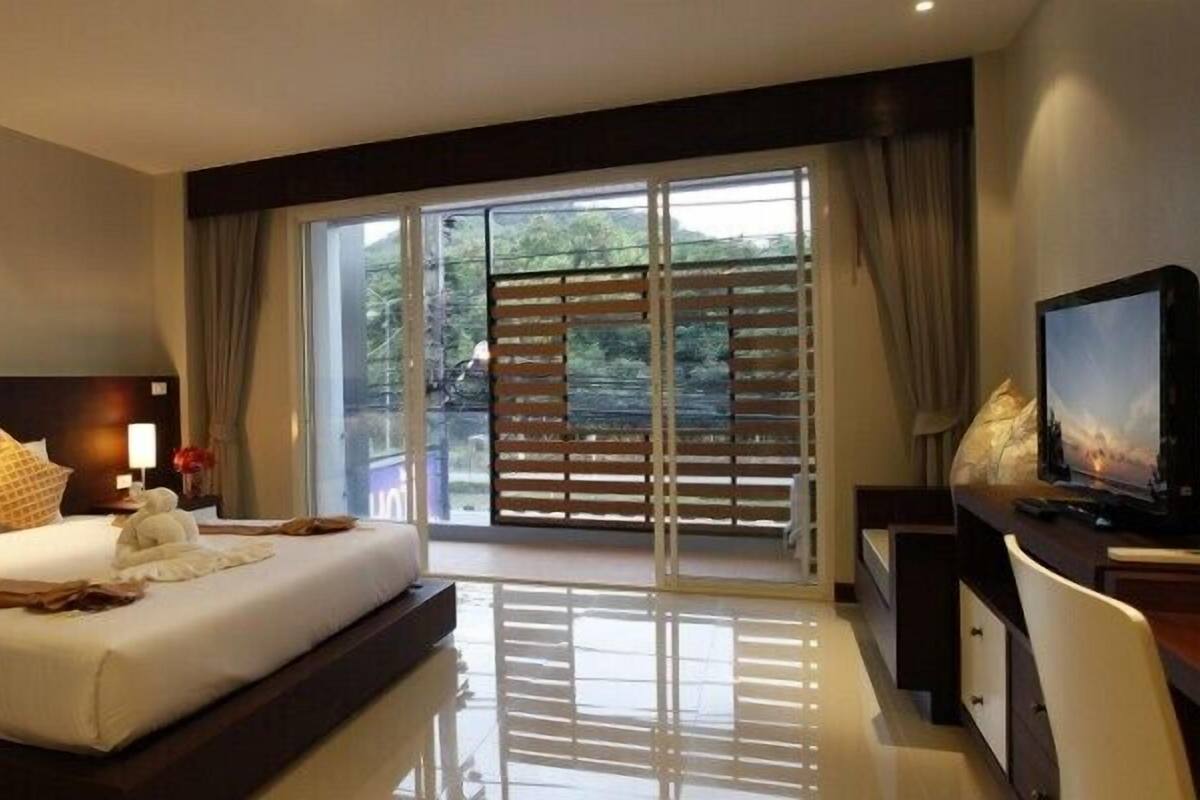 A hotel room with a large bed, a desk, a television, and a sliding glass door to the outside.