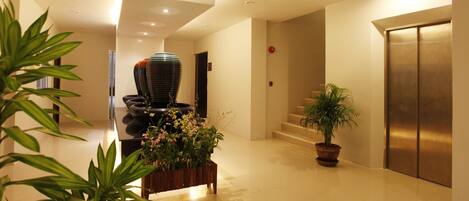 A modern hotel lobby with a central planter, a staircase, and an elevator.