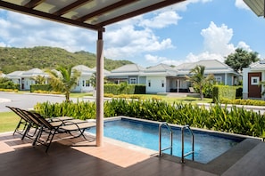 A pool area with lounge chairs, a pool, and a view of villas in the background. - Black Mountain Resort (Hua Hin)