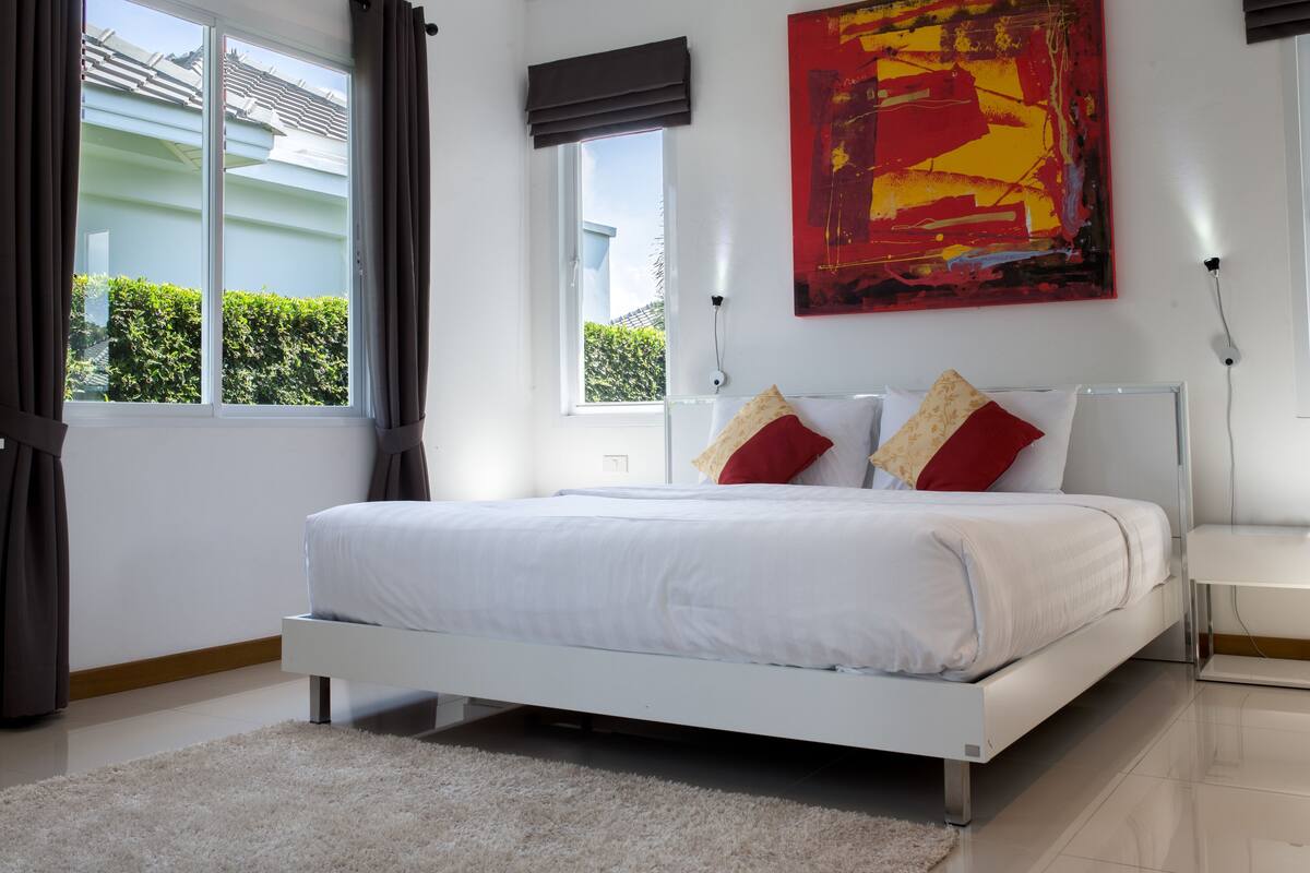 Une chambre moderne avec un lit blanc, un grand tableau abstrait et une vue sur la verdure.