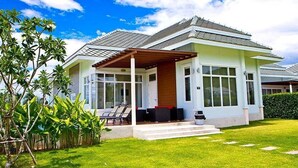 A modern house with a covered patio, a well-maintained lawn, and a large window overlooking the garden. - Black Mountain Resort (Hua Hin)