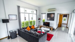 A modern living room with a grey sofa, red rug, and a TV on a wooden stand. - Black Mountain Resort (Hua Hin)
