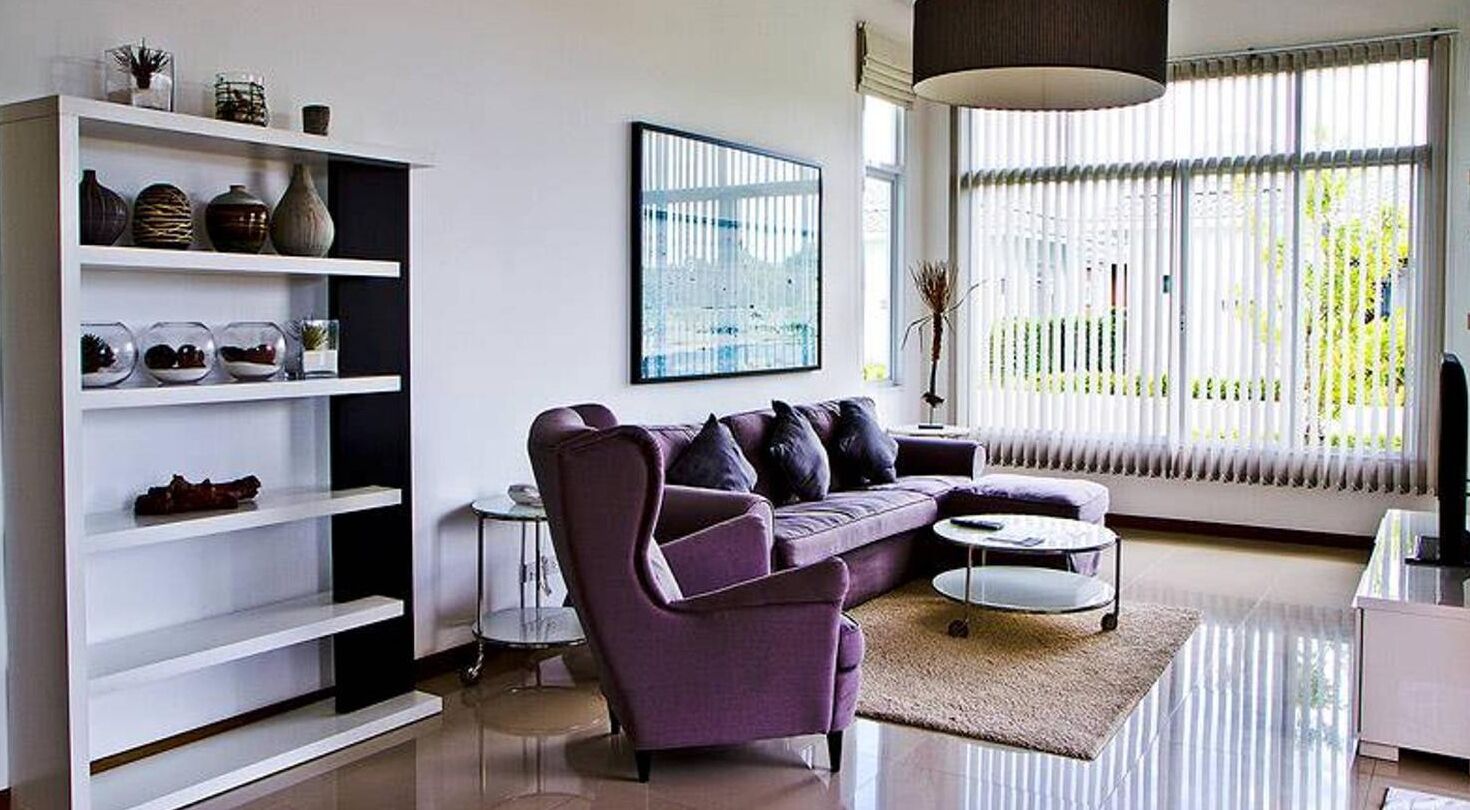 Un salon moderne avec un canapé violet, une table basse blanche et une bibliothèque agrémentée d’objets décoratifs.